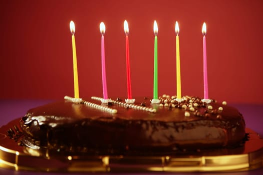 Colorful birthday light candles in a chocolate cake red background