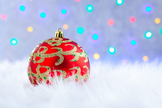 christmas bauble on white fur and colorful lights