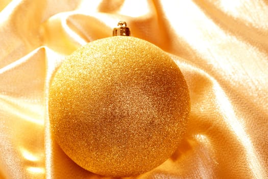 Christmas gold glitter bauble on golden fabric background