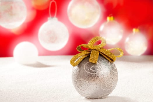 Christmas silver bauble with golden loop on snow red background