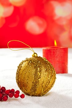 Christmas card of golden baubleand candle on snow