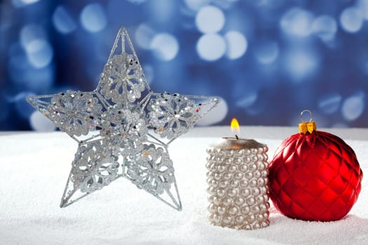 Christmas card of silver star bauble and candle on snow and blue background