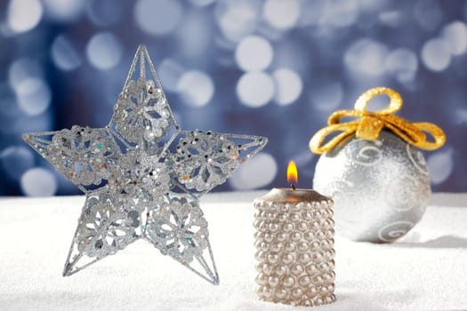 Christmas card of silver star bauble and candle on snow and blue background