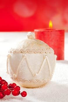Christmas card of white velvet bauble and red candle on snow background