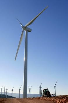 Agriculture tractor under electric wind mills in blue sky background