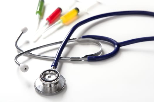 Medical still photo with blue stethoscope and colorful syringe over white