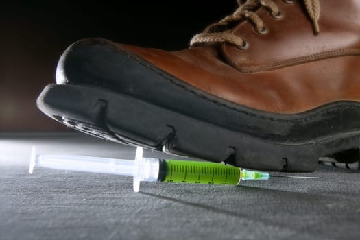 Boot treading a green liquid syringe, leaving drug addiction metaphor