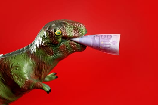 Toy dinosaur with euro note in its yaws over red background