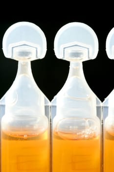 plastic white macro ampoule of orange medicine over black background