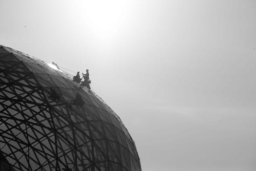 Climber cleaning mirror glass dome building  climbing ropes
