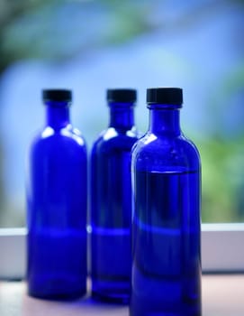 Three Blue glass body oil bottles in bathroom window