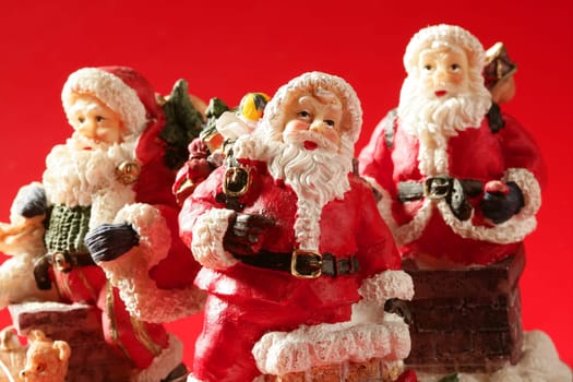 Three Santa Claus figurines over red background, studio shot