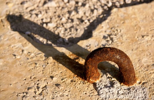 aged rusty shackle in dock concrete stone, with long shadow