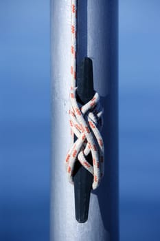 Marine rope, knot arround a steel pole, blue water background