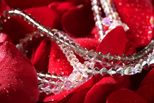 Shiny jewelry over bed or red rose petals