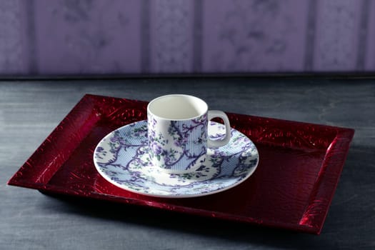 Tea cup victorian style on red indian tray, purple wallpaper background