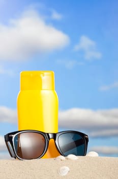 Tube with sun protection and sunglasses on beach and blue sky in background