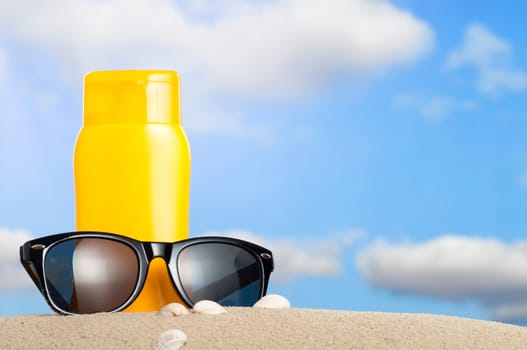 Tube with sun protection and sunglasses on beach and blue sky in background