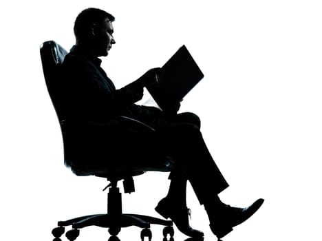 one caucasian business man sitting in armchair reading ancient book silhouette Full length in studio isolated on white background