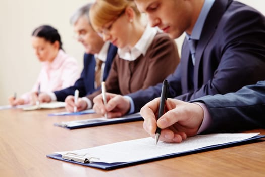 Row of business people making notes with focus on hand holding pen