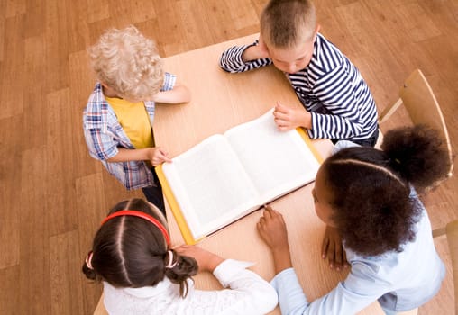 Above view of pupils looking at page of encyclopaedia at reading lesson