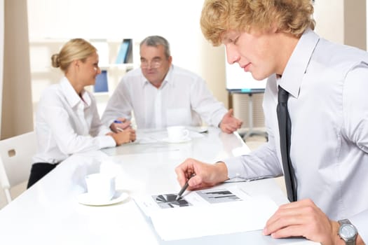 Portrait of confident businessman thinking over business plan with communicating partners at background