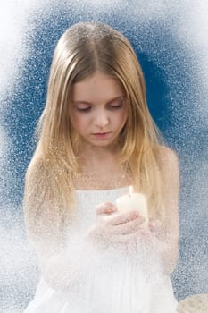 Image of praying girl looking at burning candle in her hands behind frosty window