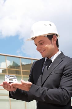 Portrait of confident foreman in helmet holding toy house on palm
