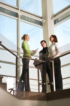Two girls and man are talking in the building with glassy walls