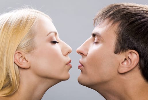 Two amorous people showing love and affection by mutual air kiss over grey background