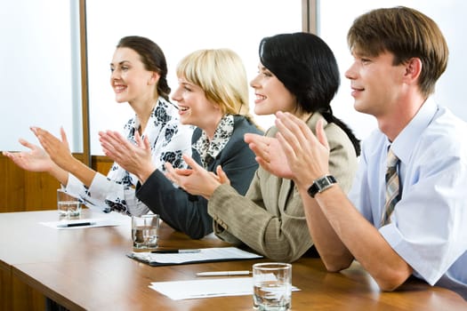 Successful applauding young people sitting at the table in the office