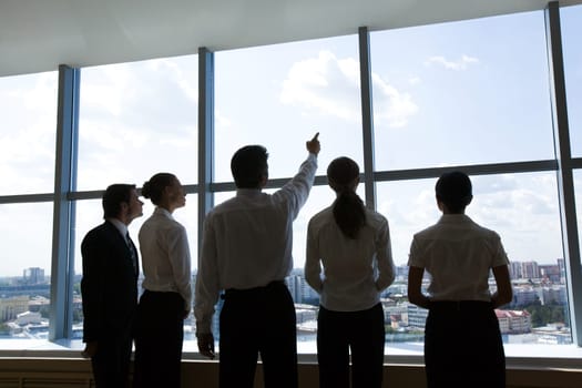 Rear view of business group standing in row and looking through window with their leader smiling at camera