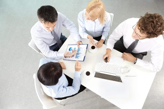 Group of business partners listening to mature woman pointing at document at meeting