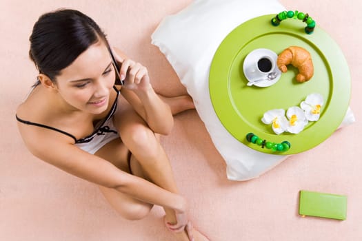 Teenage girl sitting on bed and talking on cellular phone in the morning