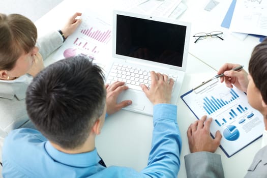 Three business people sitting at table with papers and laptop and planning