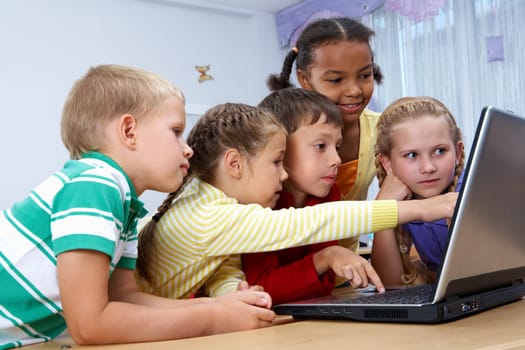 Portrait of smart schoolgirls and schoolboys looking at the laptop