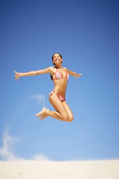 Portrait of joyful girl leaping on sandy beach during summer vacation and laughing