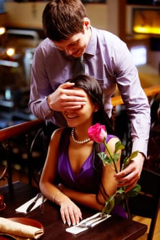 Handsome man shuts woman's eyes by hand and gives rose