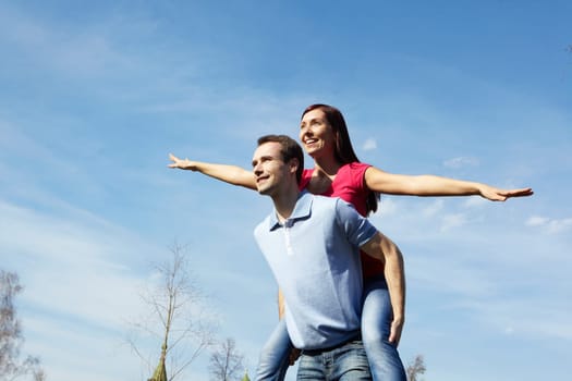 Happy man giving piggyback to his wife outdoors against blue sky