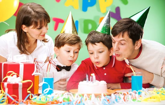 Portrait of family blowing together at the holiday candles on the cake