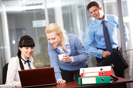 Two confident employees looking at monitor while while their boss entering office