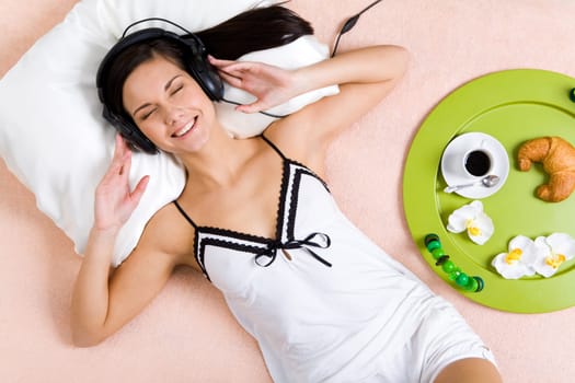 Pretty girl listening to music in headphones and smiling while lying on bed