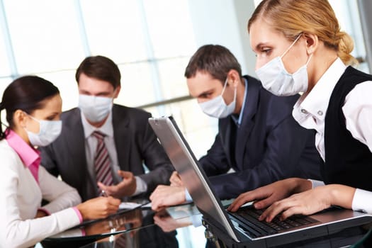 Serious businesswoman in protective mask looking at screen of laptop in working environment