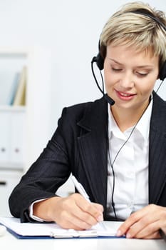 Portrait of young secretary with headset sitting at table and making notes