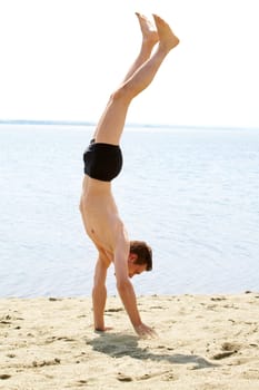 Energetic guy standing on arms on sand with outstretched legs