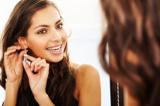 Image of pretty female looking in mirror and putting on earrings
