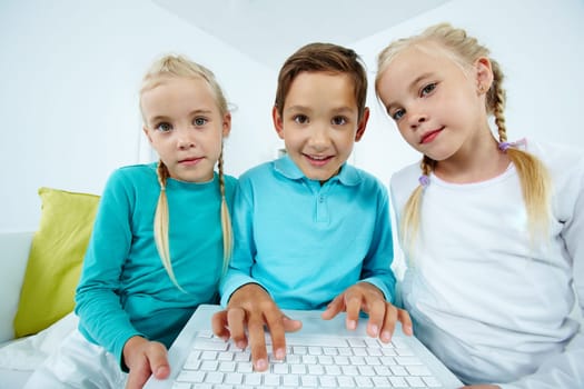 Smart schoolboy typing between twin girls