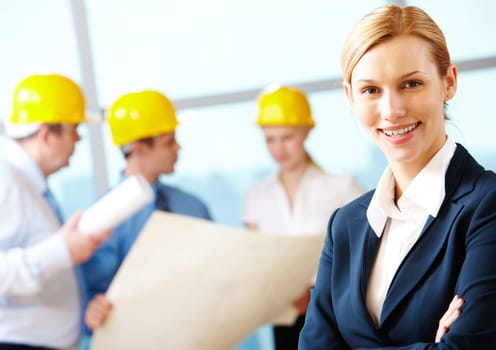 Portrait of beautiful architect folding arms on the background of workers