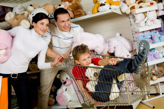 Image of cute kid showing something to his parents in shop while they looking at it with smiles