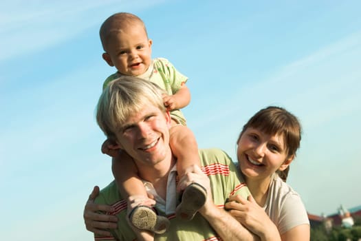 Photo of father with baby and mother looking at camera in open air